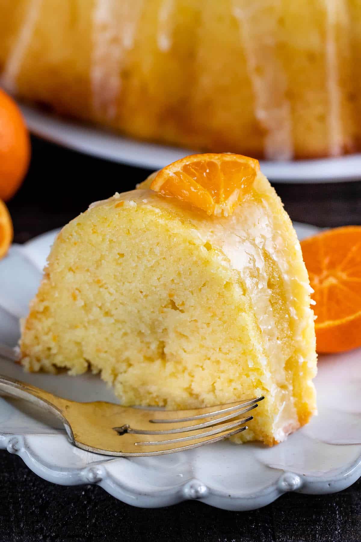 orange bundt cake with sliced oranges and icing on top on a white plate.