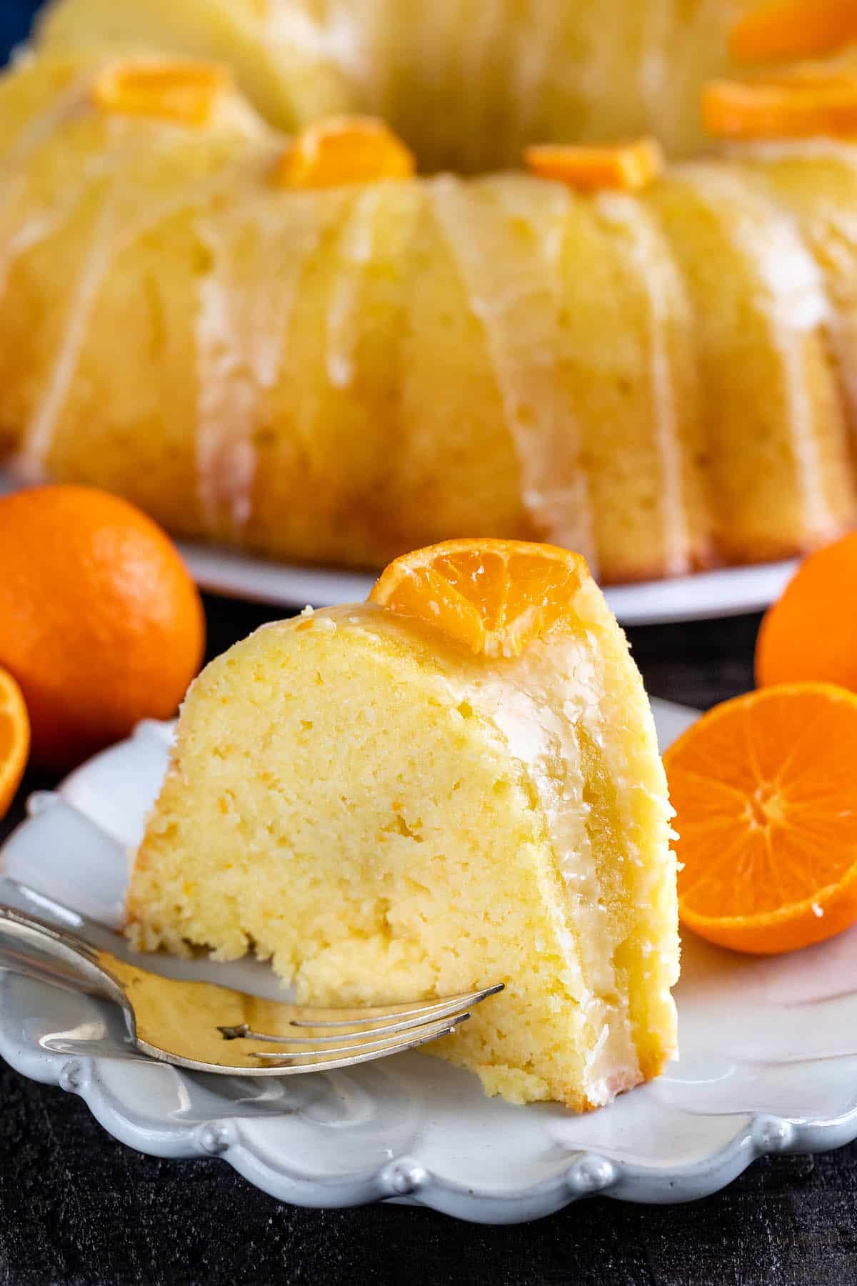 orange bundt cake with sliced oranges and icing on top on a white plate.