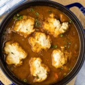 chicken and dumplings in brown soup in a black bowl.