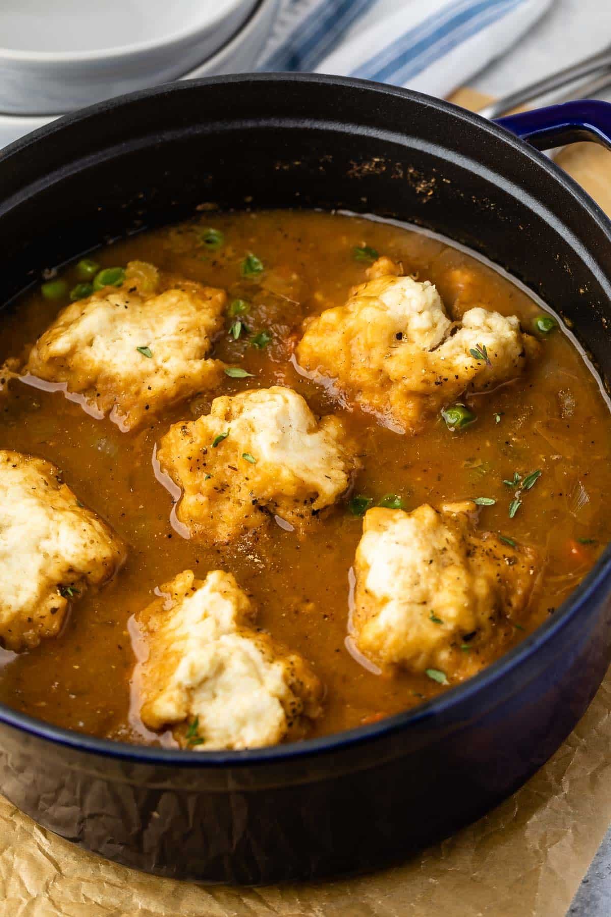 chicken and dumplings in brown soup in a black bowl.