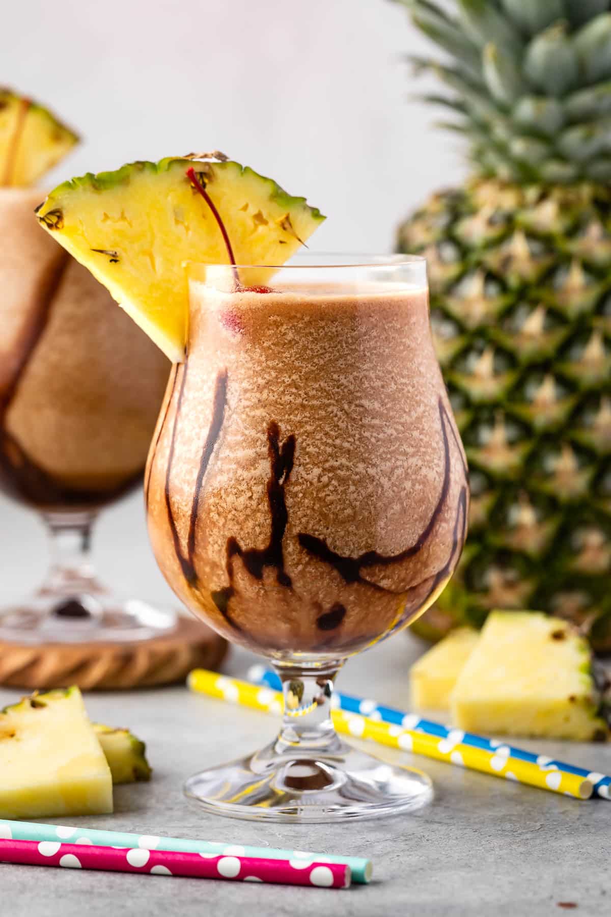 chocolate pina colada in a clear glass with a pineapple and cherry on the rim.
