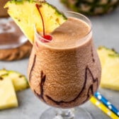 chocolate pina colada in a clear glass with a pineapple and cherry on the rim.