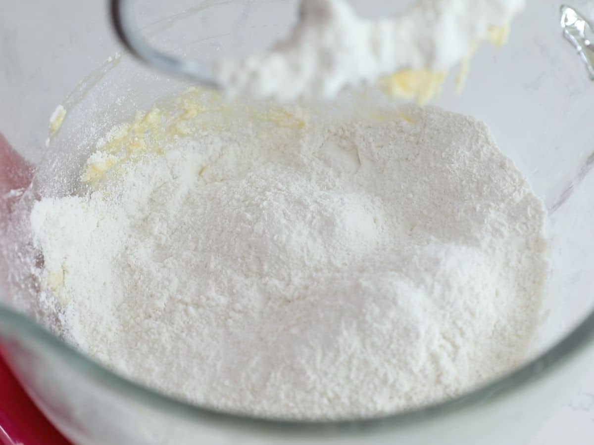 flour over butter and sugar mixture in glass bowl of stand mixer.