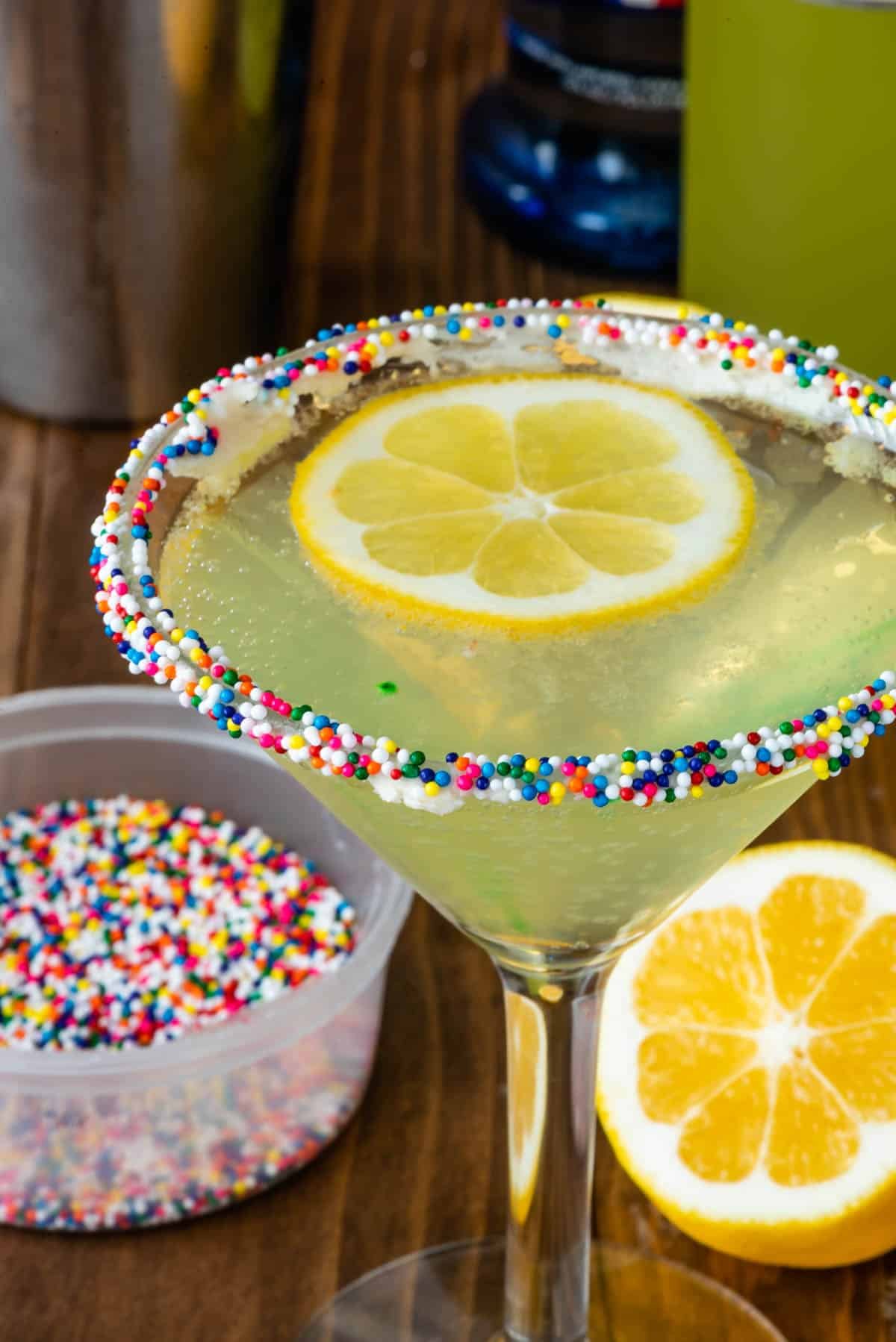 yellow in a clear glass with sprinkles on the rim and sliced lemons in the glass.