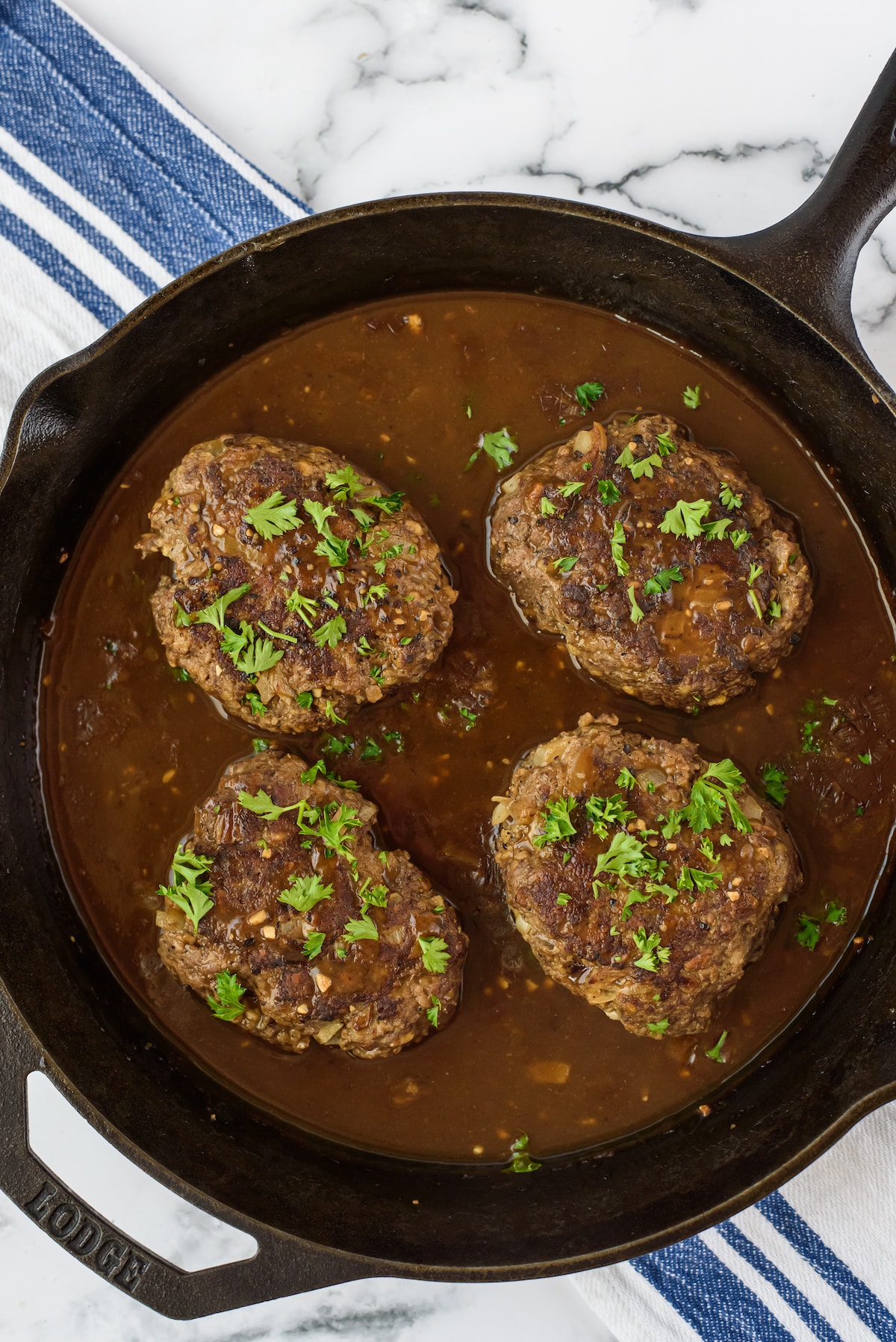 four steaks in sauce in a black pan.