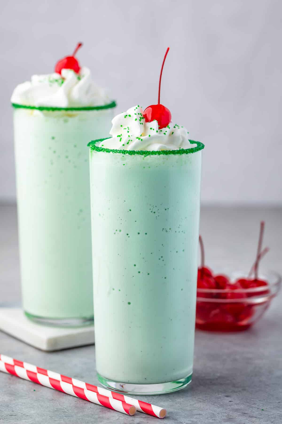 green shake in a clear glass topped with whipped cream and a cherry.