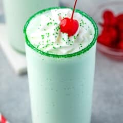 green shake in a clear glass topped with whipped cream and a cherry.