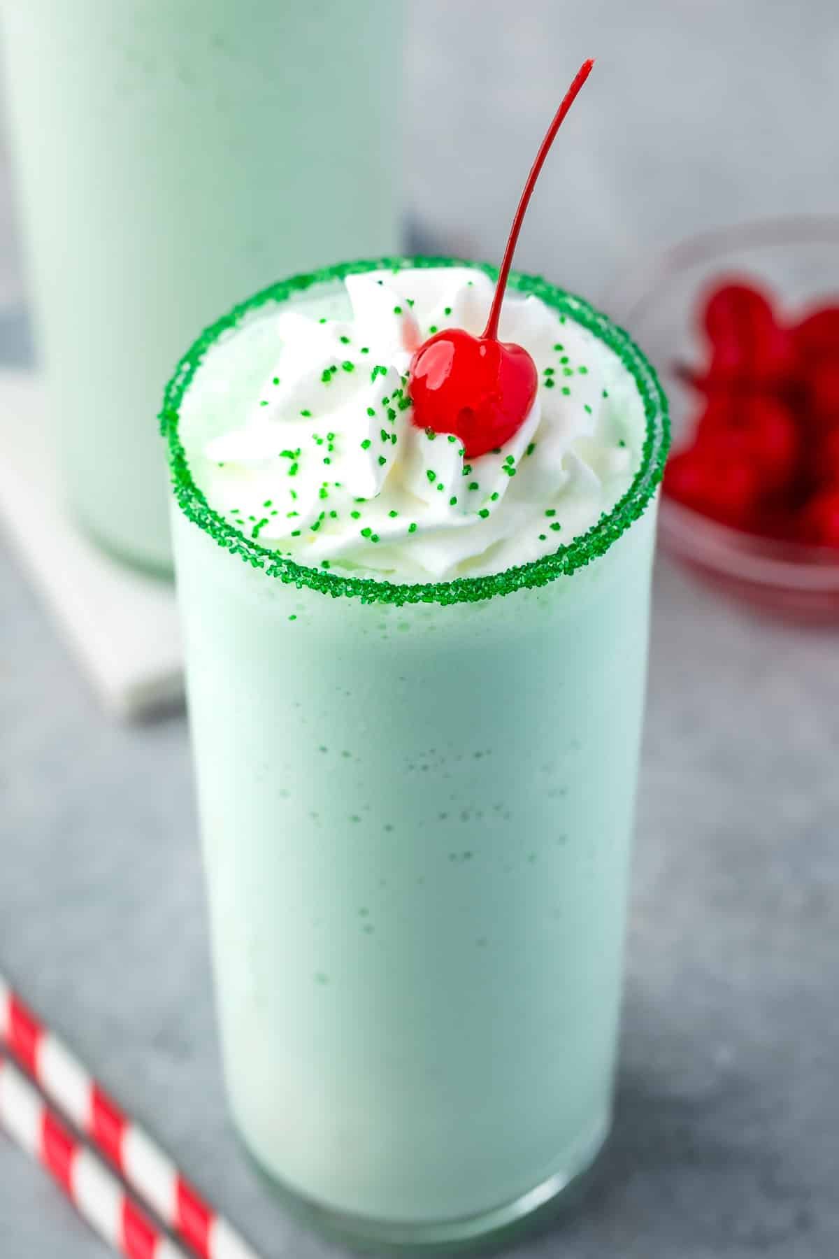 green shake in a clear glass topped with whipped cream and a cherry.