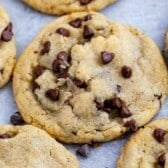 Close-up of several freshly baked small batch chocolate chip cookies on a sheet of parchment paper. The cookies are golden brown with visible melted chocolate chips throughout.