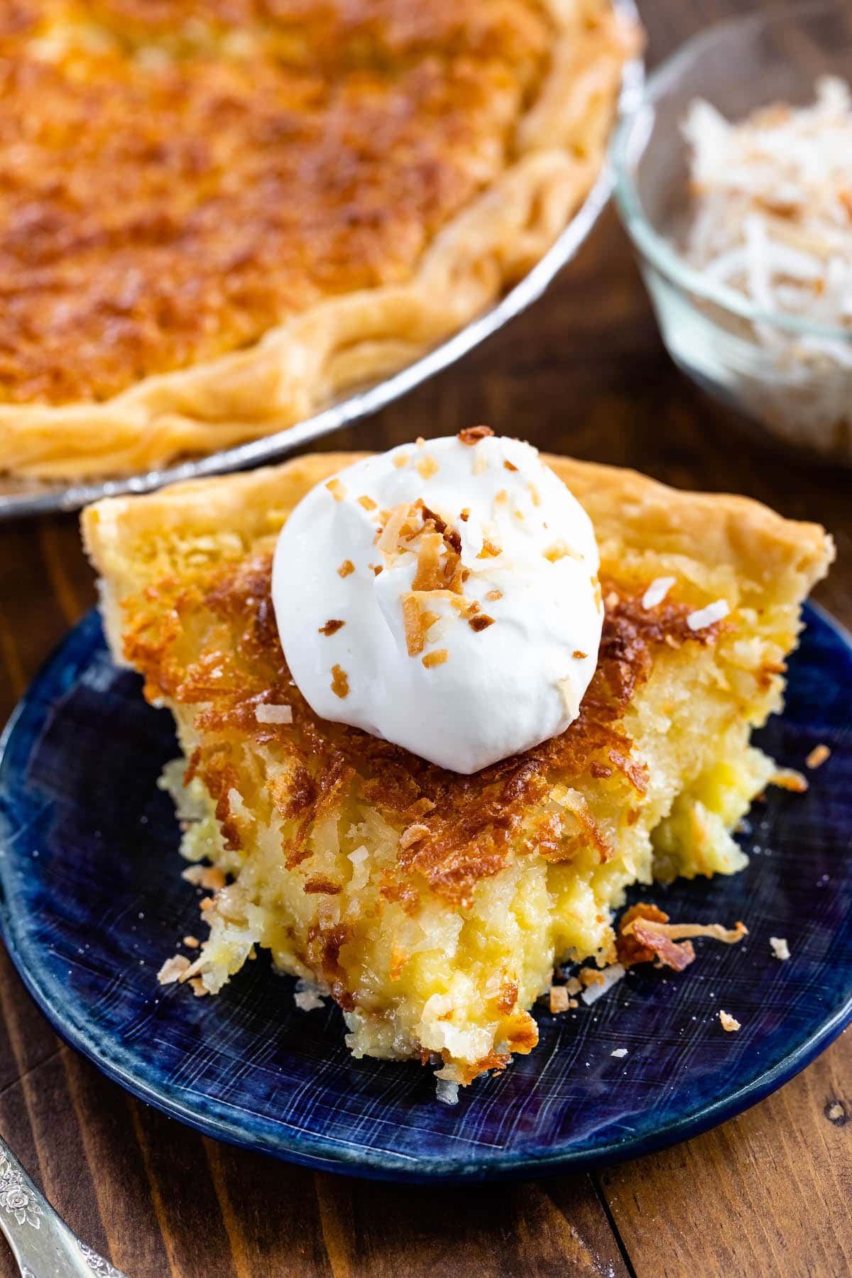 slice of coconut pie on a blue plate with whipped cream on top.