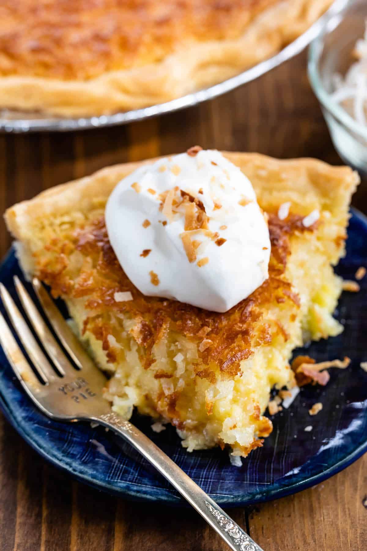 slice of coconut pie on a blue plate with whipped cream on top.