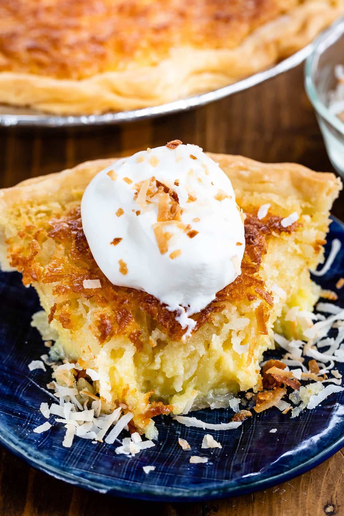 slice of coconut pie on a blue plate with whipped cream on top.