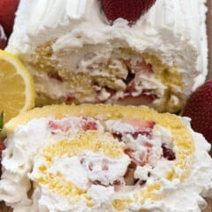 cake roll covered in white frosting with lemon slices and strawberries laid on top.