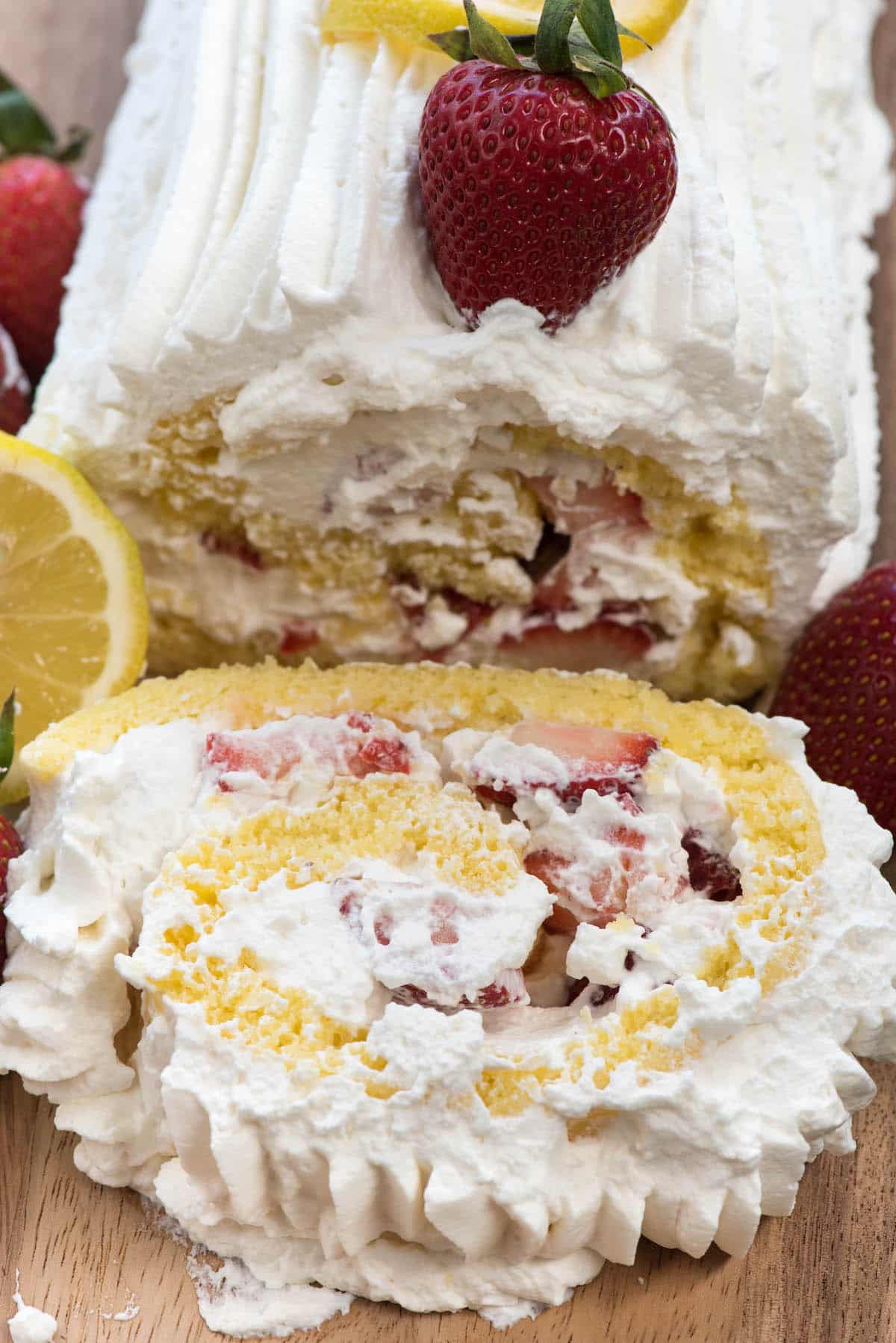 cake roll covered in white frosting with lemon slices and strawberries laid on top.