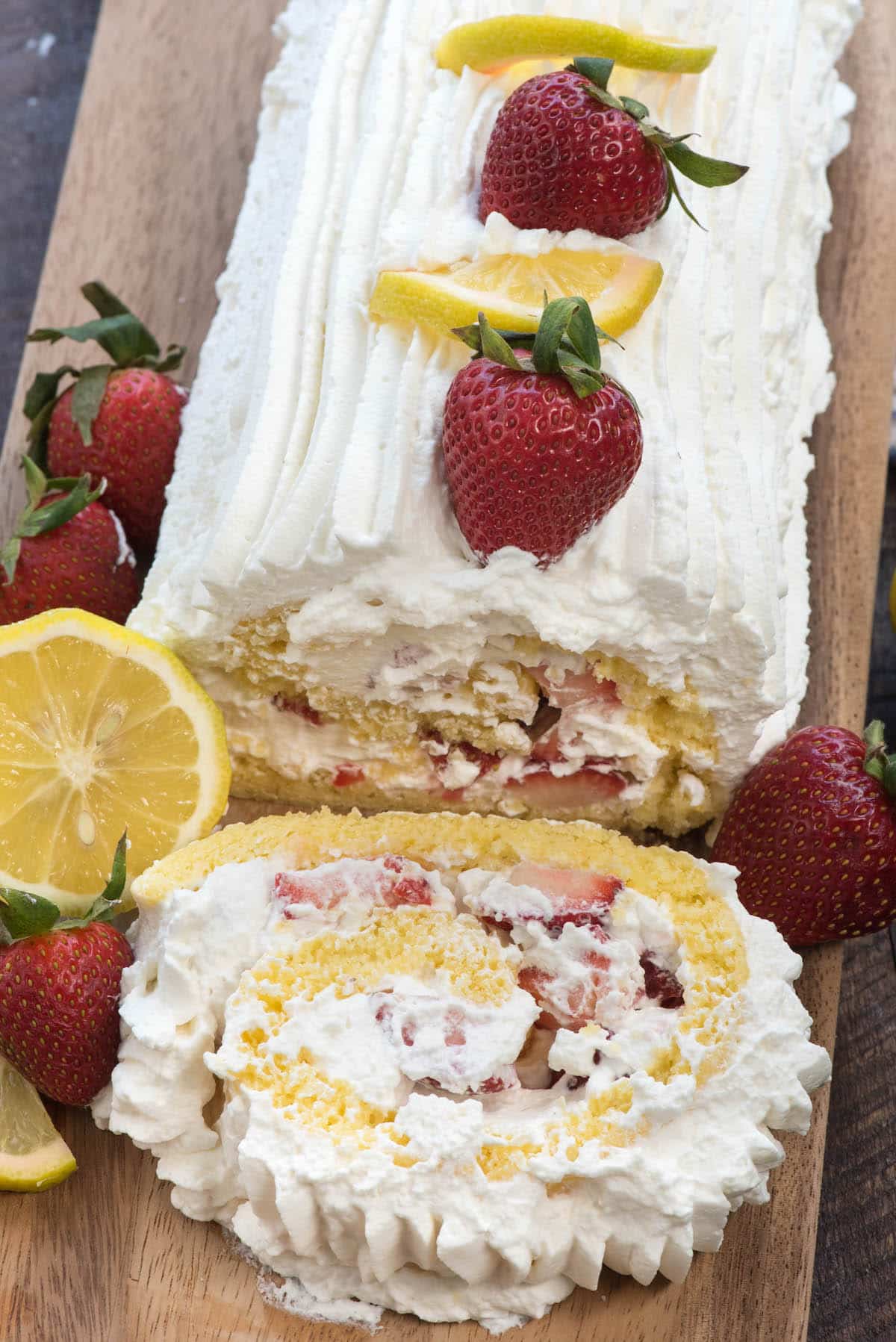 cake roll covered in white frosting with lemon slices and strawberries laid on top.