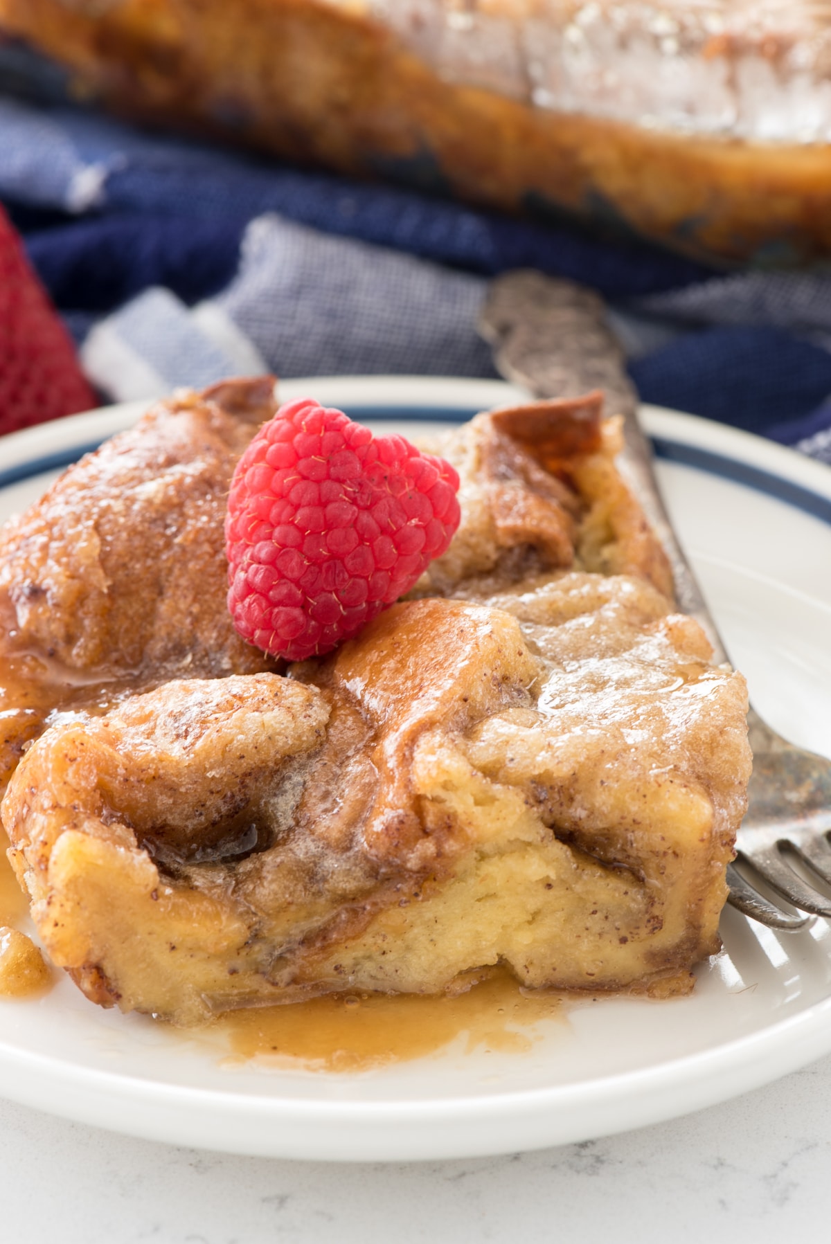 french toast casserole with syrup on white plate with fork and raspberry