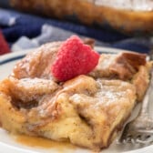 french toast casserole with syrup on white plate with fork and raspberry