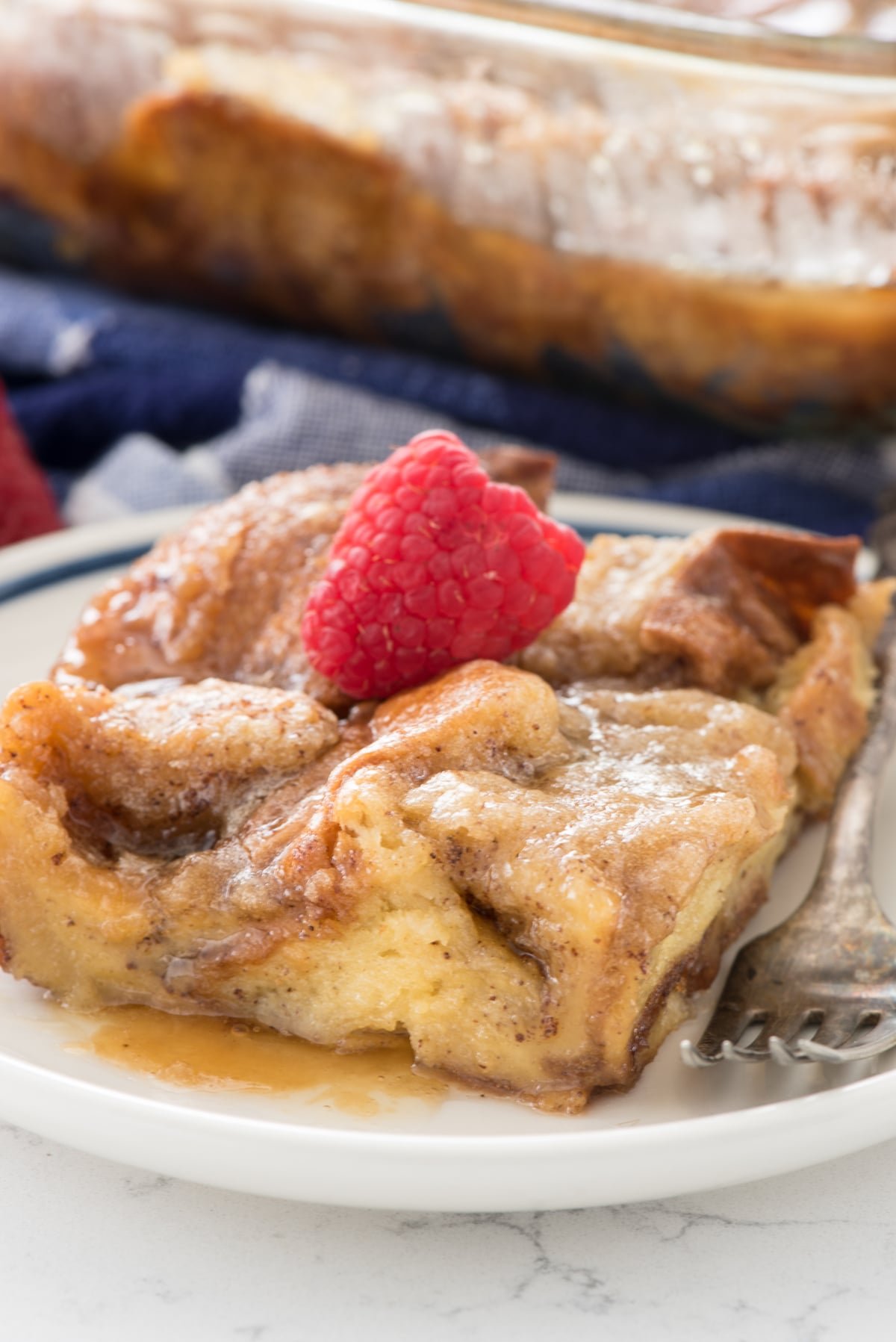 french toast casserole with syrup on white plate with fork and raspberry