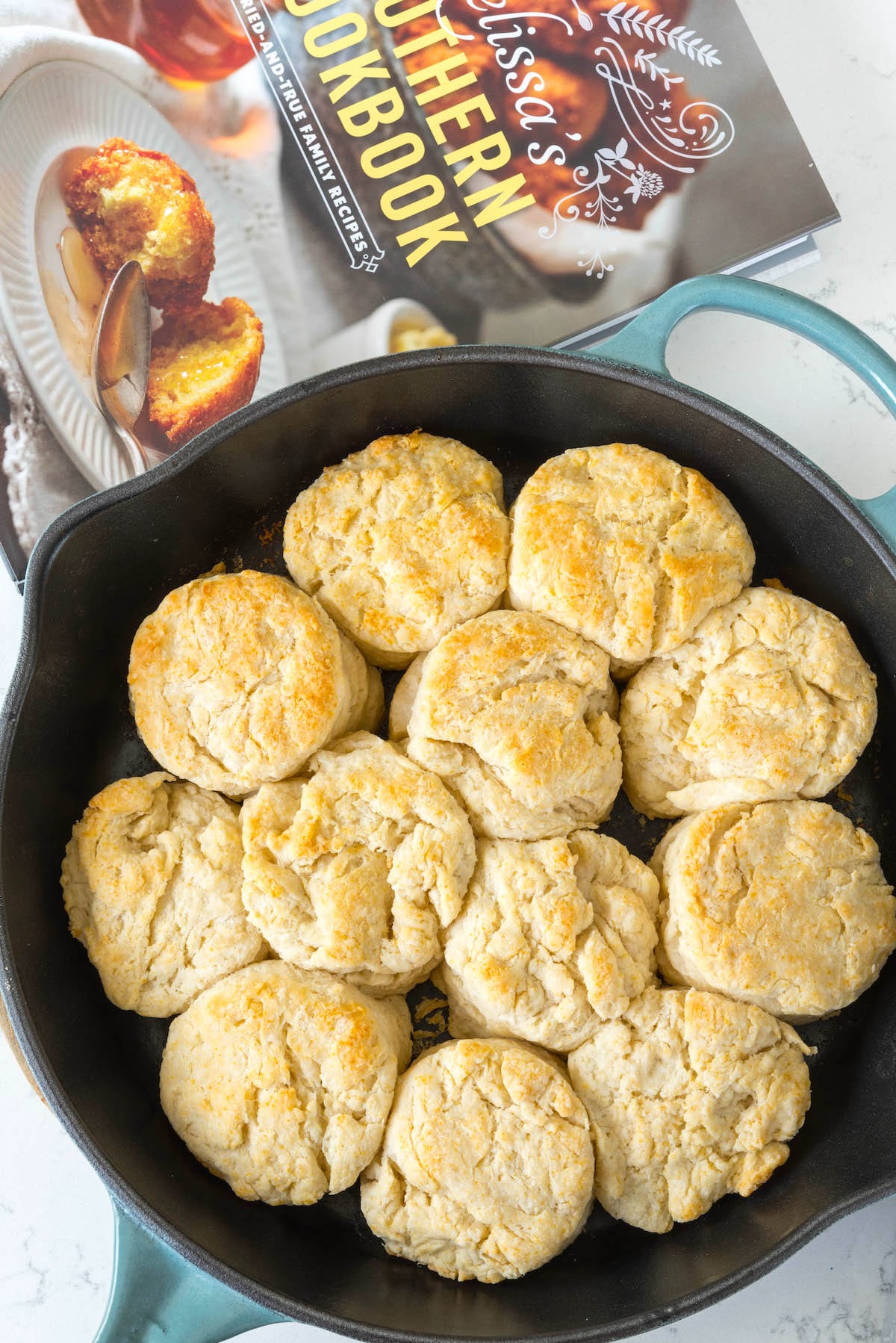 cooked biscuits in a black pan next to a cookbook.