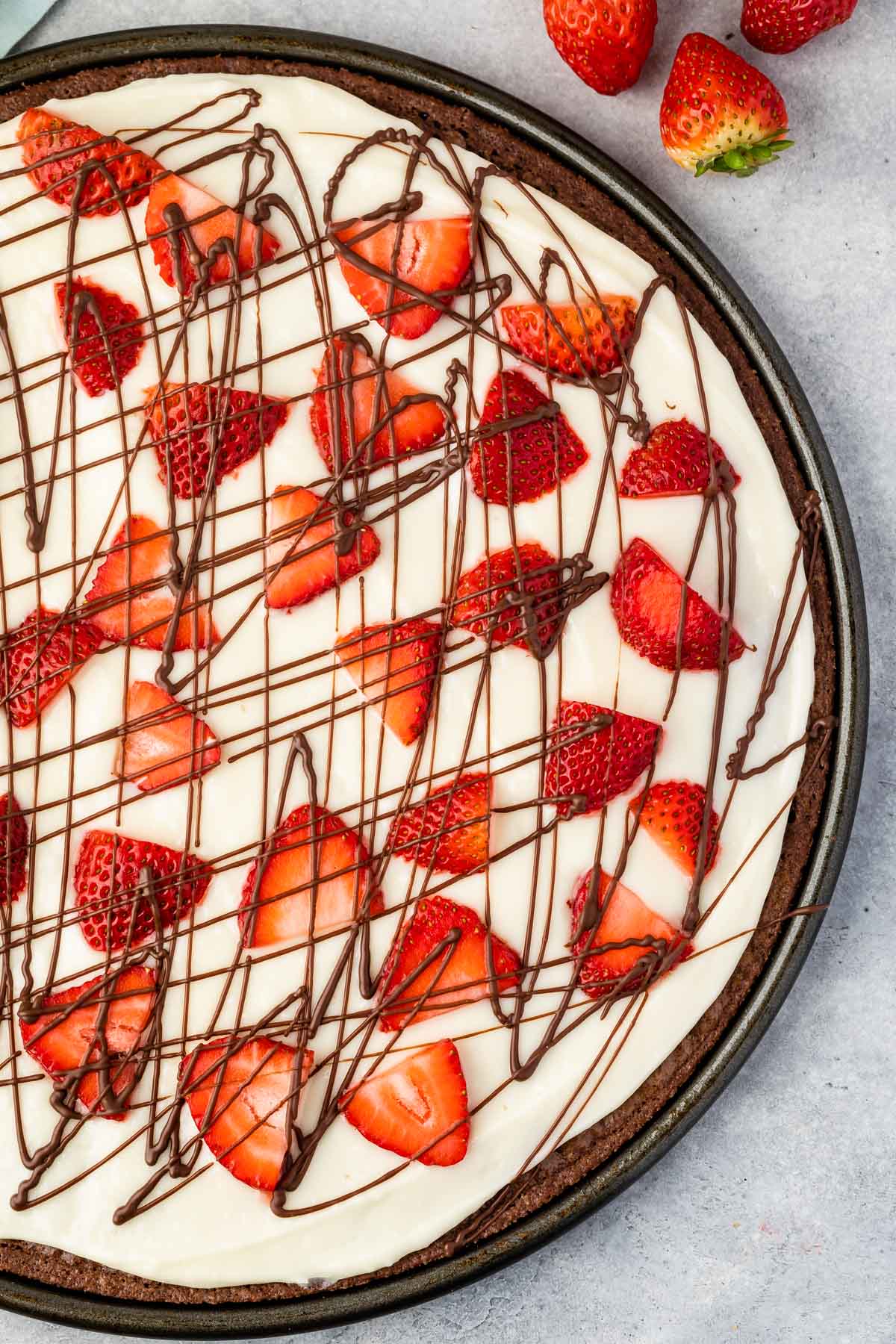 brownie in the shape of a pizza topped with frosting and chocolate sauce and strawberries.