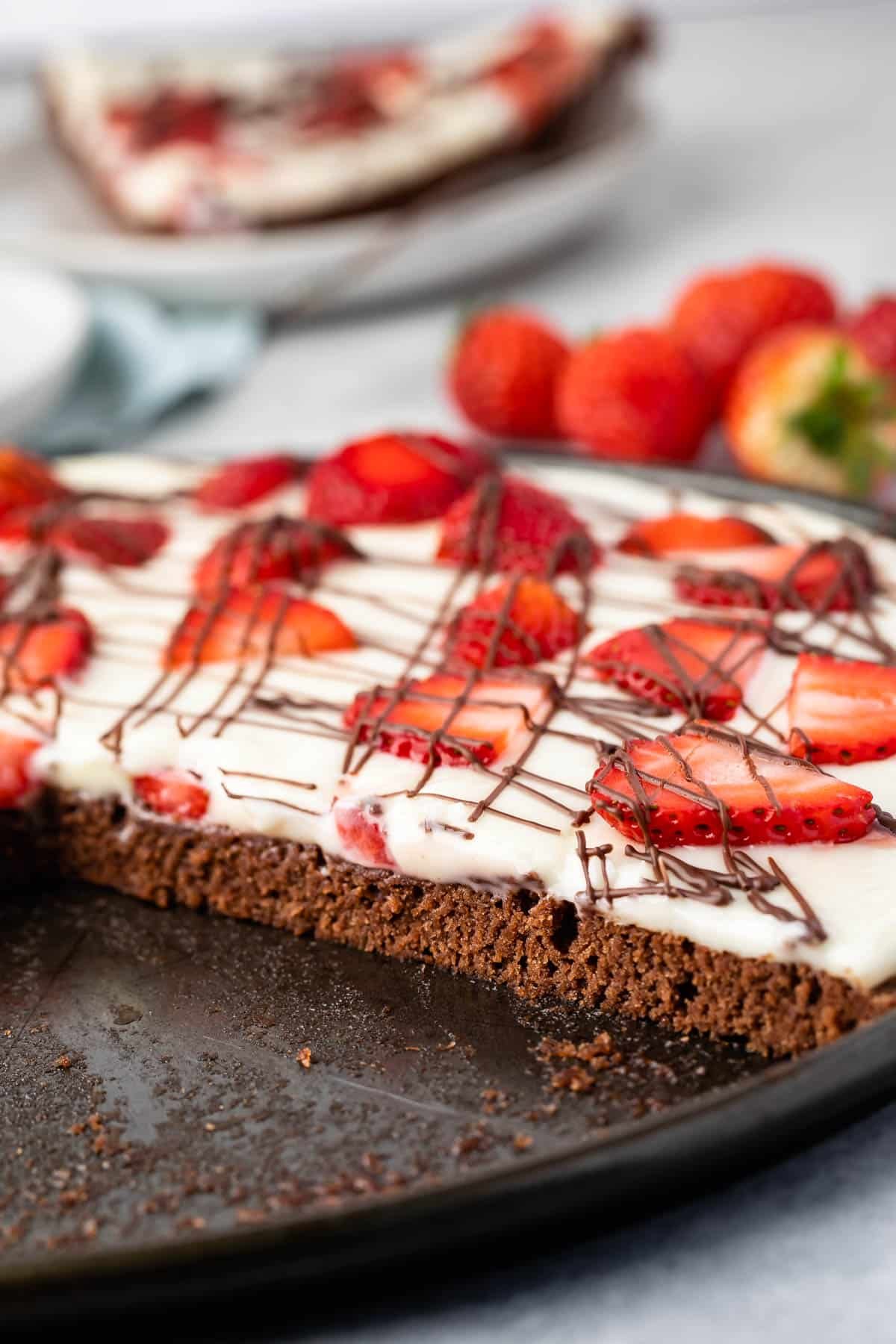 brownie in the shape of a pizza topped with frosting and chocolate sauce and strawberries.