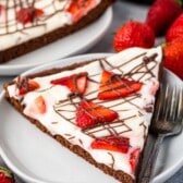 brownie in the shape of a pizza topped with frosting and chocolate sauce and strawberries.