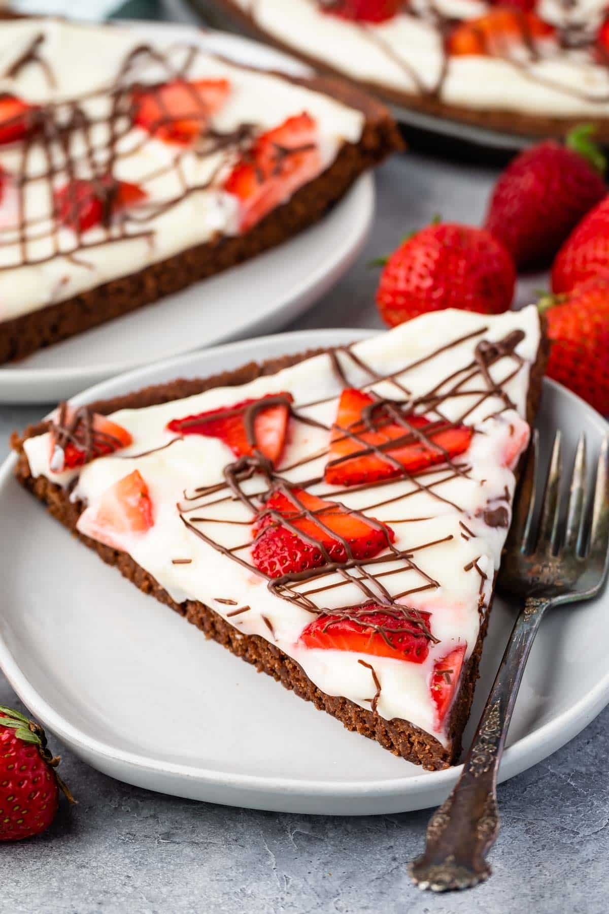 brownie in the shape of a pizza topped with frosting and chocolate sauce and strawberries.