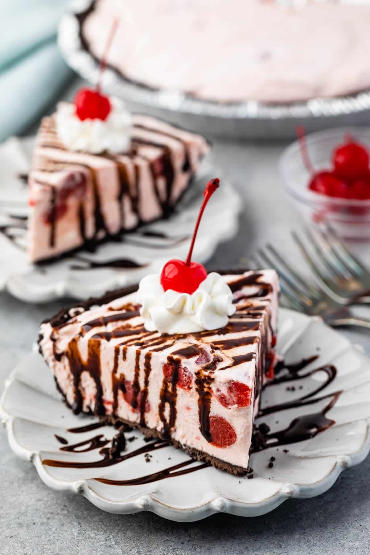 pink slice of pie covered in chocolate sauce, whipped cream and a cherry.