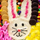 bunny shaped out of frosting and surrounded by jelly beans, marshmallows and oreos with words on the image.