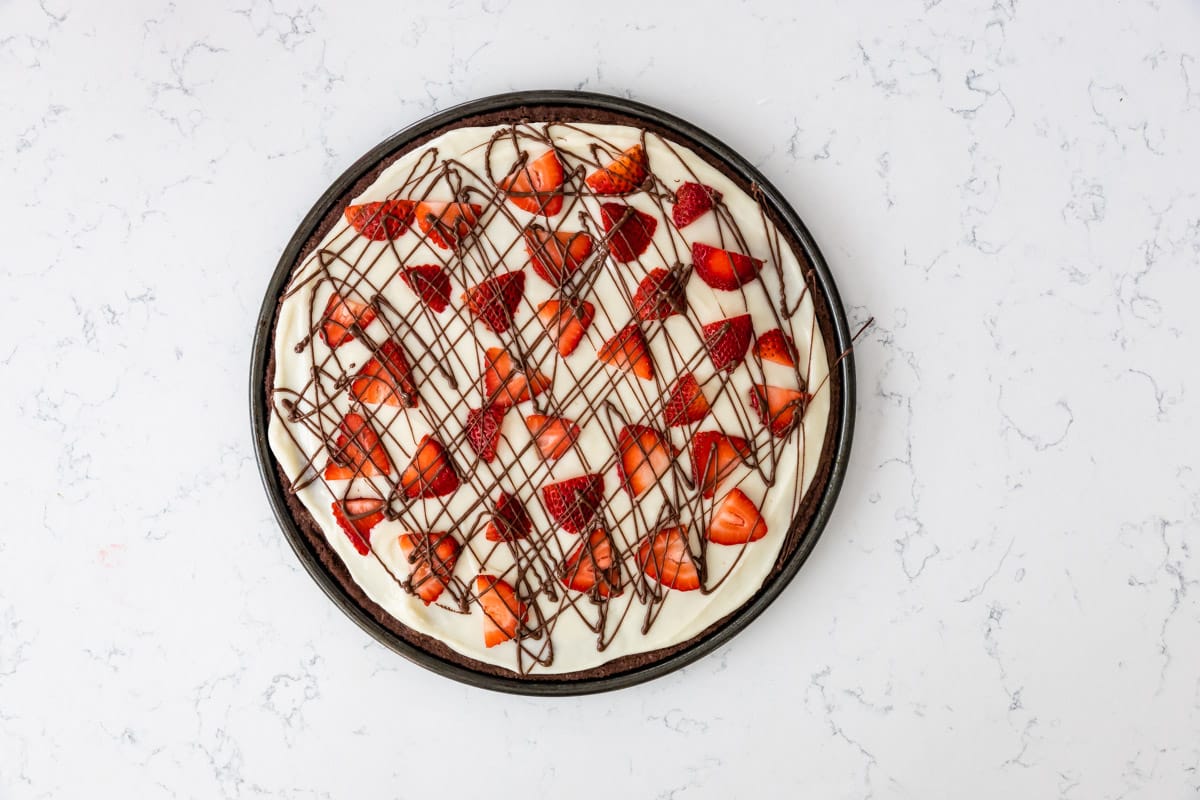 brownie in the shape of a pizza topped with frosting and chocolate sauce and strawberries.
