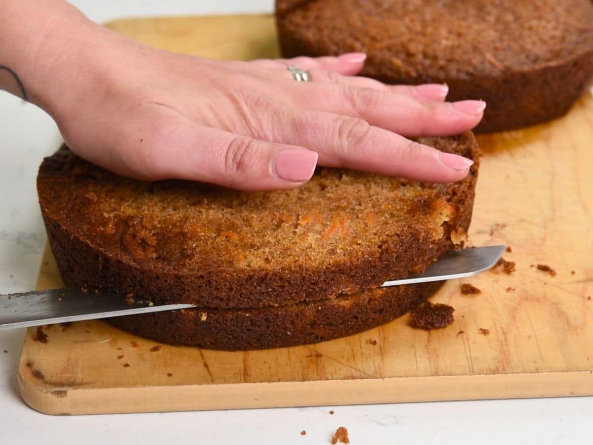 hand on top of cake layer with knife cutting it.