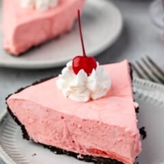 slice of pink pie on oreo crust with whipped cream and a cherry on top.