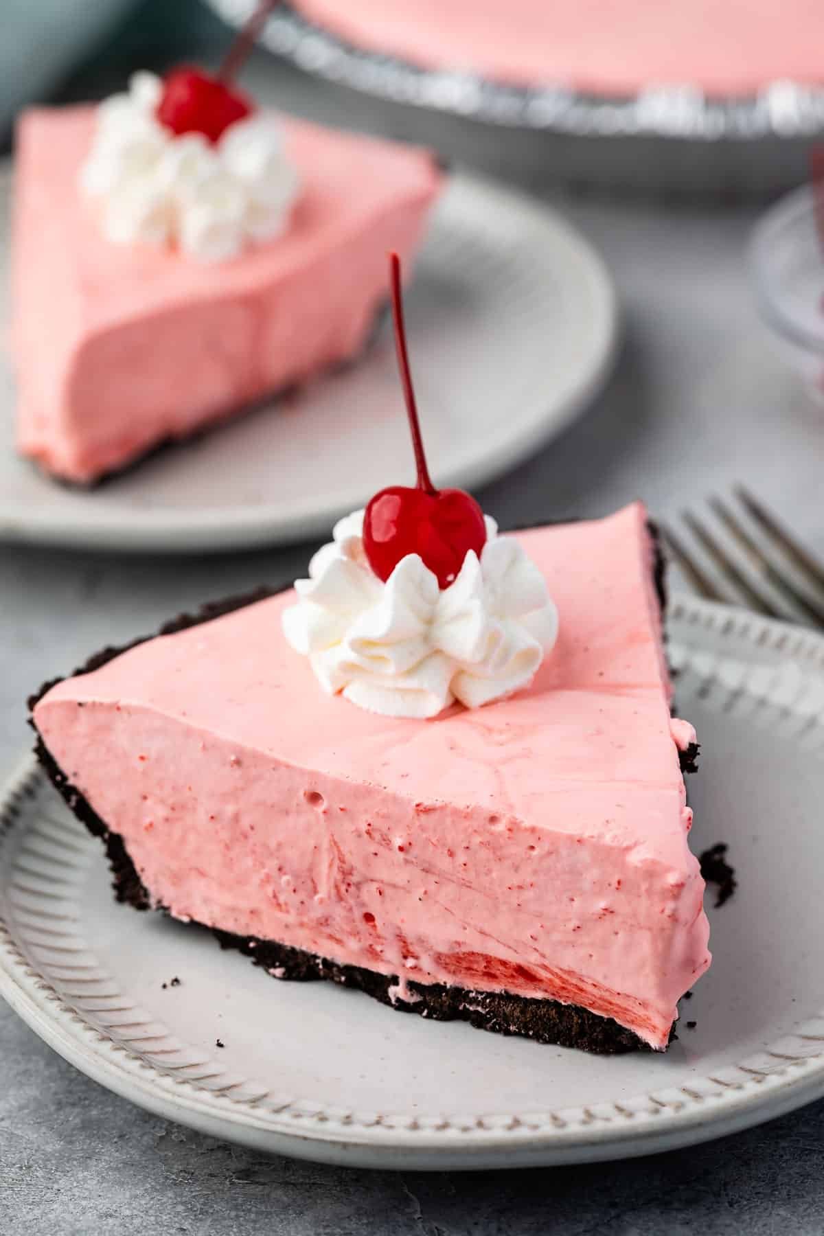 slice of pink pie on oreo crust with whipped cream and a cherry on top.