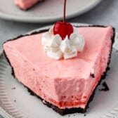 slice of pink pie on oreo crust with whipped cream and a cherry on top.