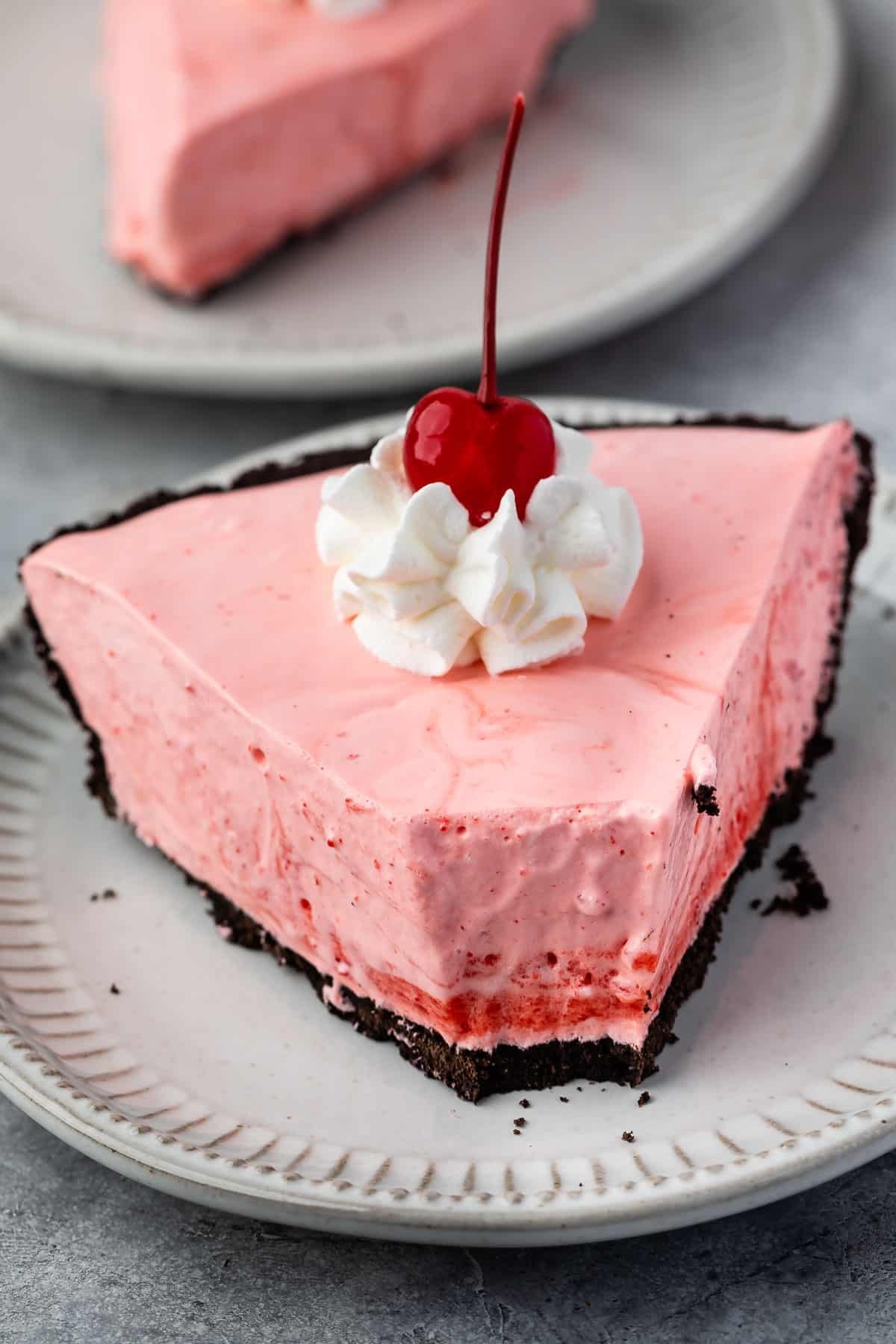 slice of pink pie on oreo crust with whipped cream and a cherry on top.