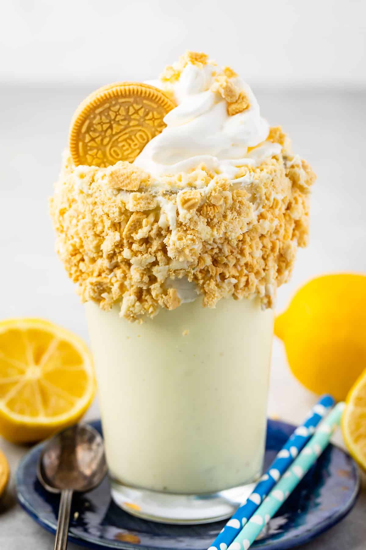 lemon milkshake in a clear glass and crushed golden oreos around the rim of the glass.