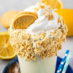 lemon milkshake in a clear glass and crushed golden oreos around the rim of the glass.