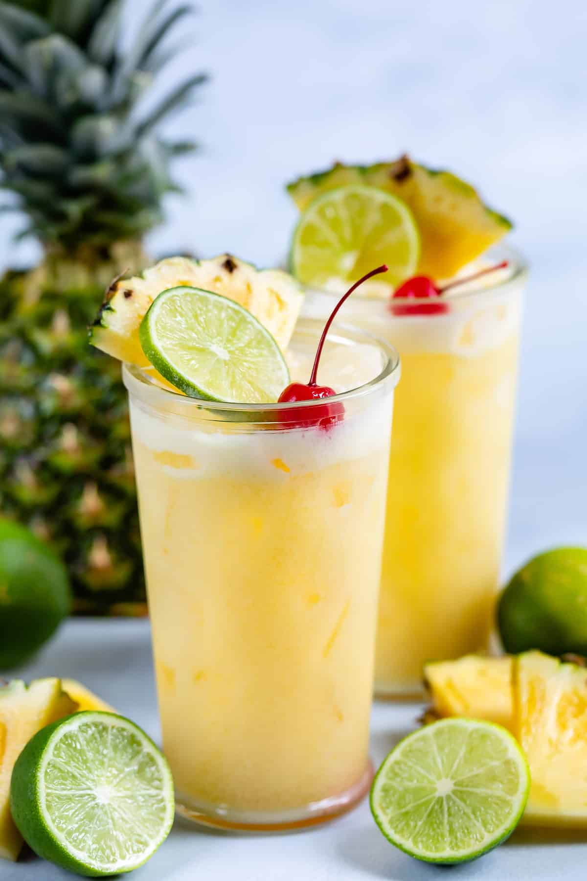 yellow cocktail in a clear glass with a cherry, lime and pineapple slice in the drink.