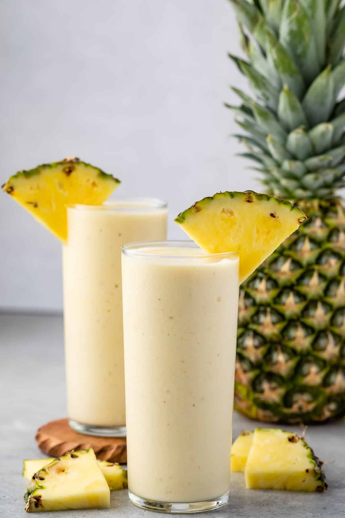 yellow pineapple smoothie in a tall clear glass with a pineapple slice on the rim.