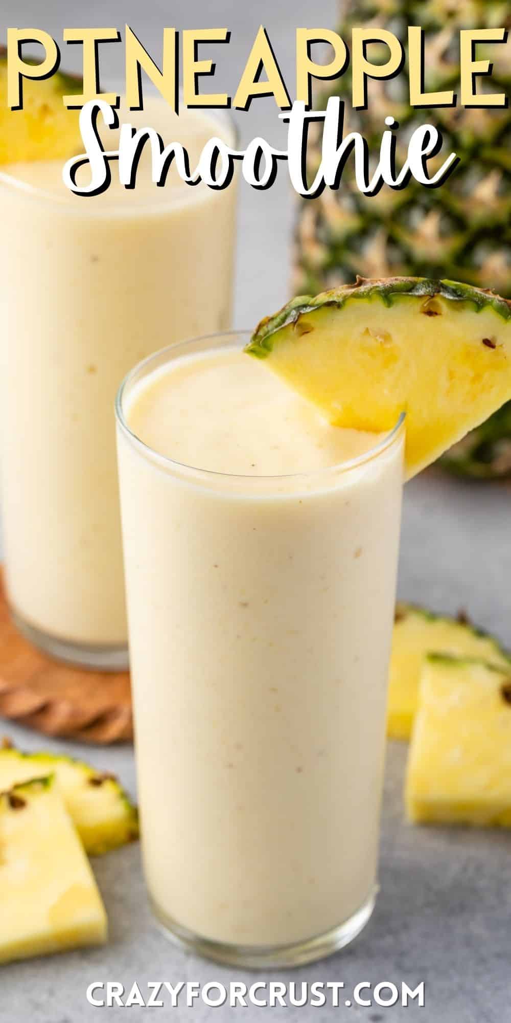yellow pineapple smoothie in a tall clear glass with a pineapple slice on the rim with words on the image.