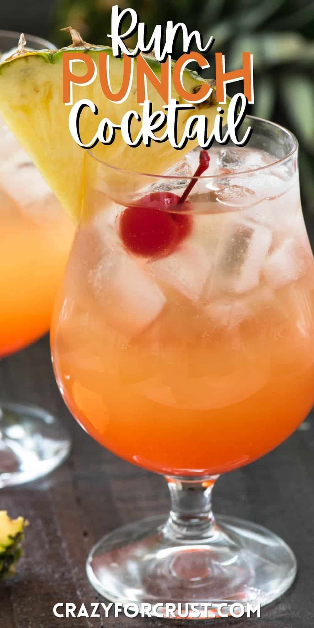 orange cocktail in a clear glass with a cherry and pineapple slice on the rim with words on the image.