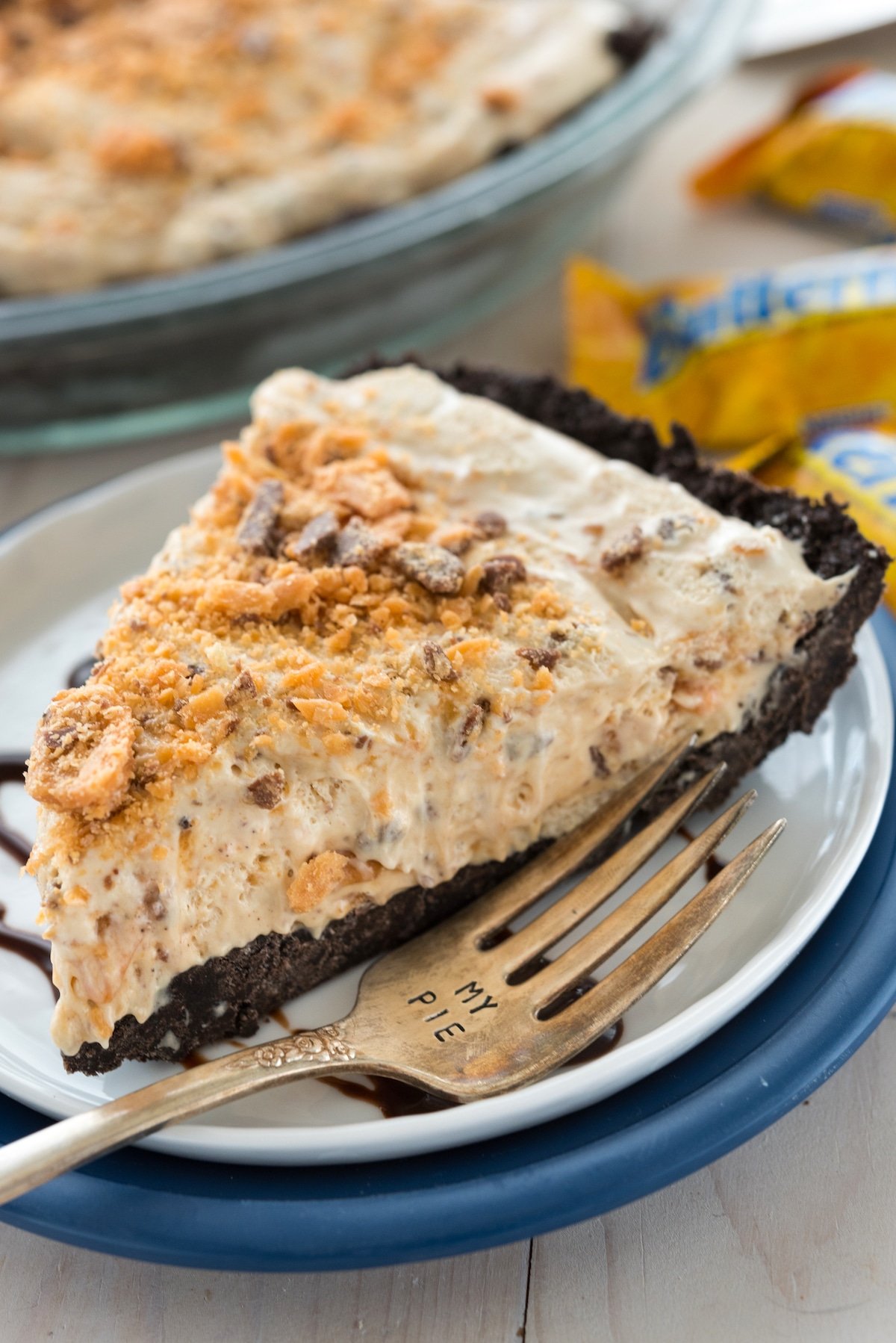 butterfinger pie on a white plate covered in chocolate sauce.