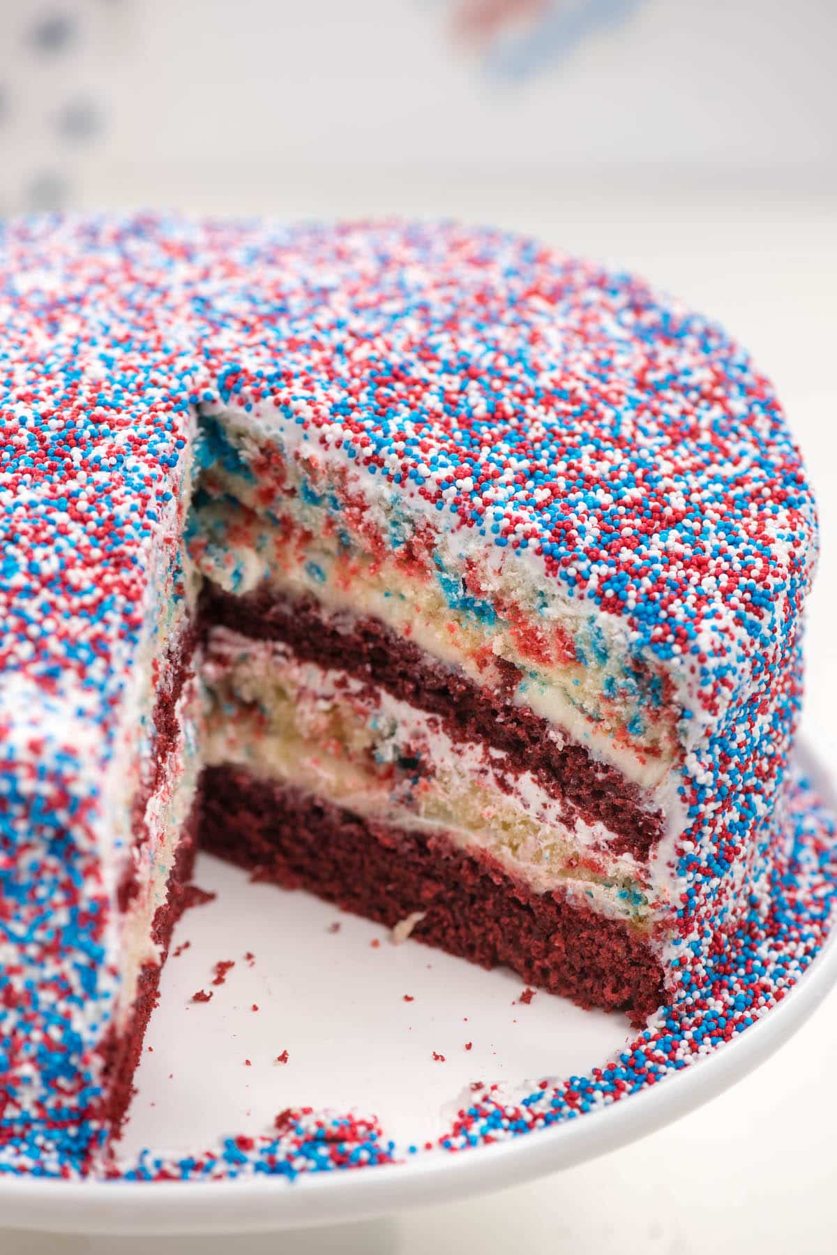 yellow and red layered cake covered in patriotic sprinkles on a white plate.