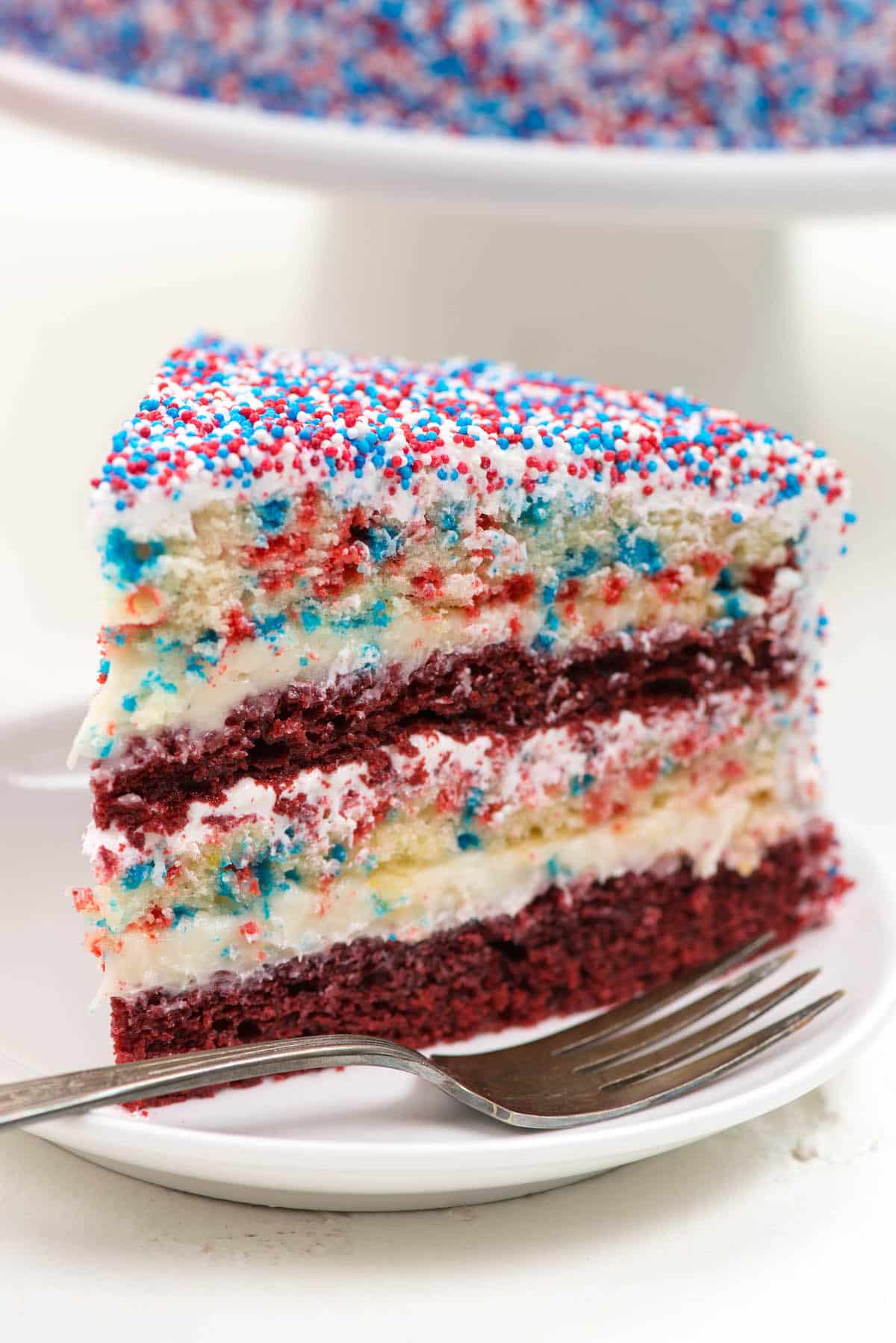 yellow and red layered cake covered in patriotic sprinkles on a white plate.