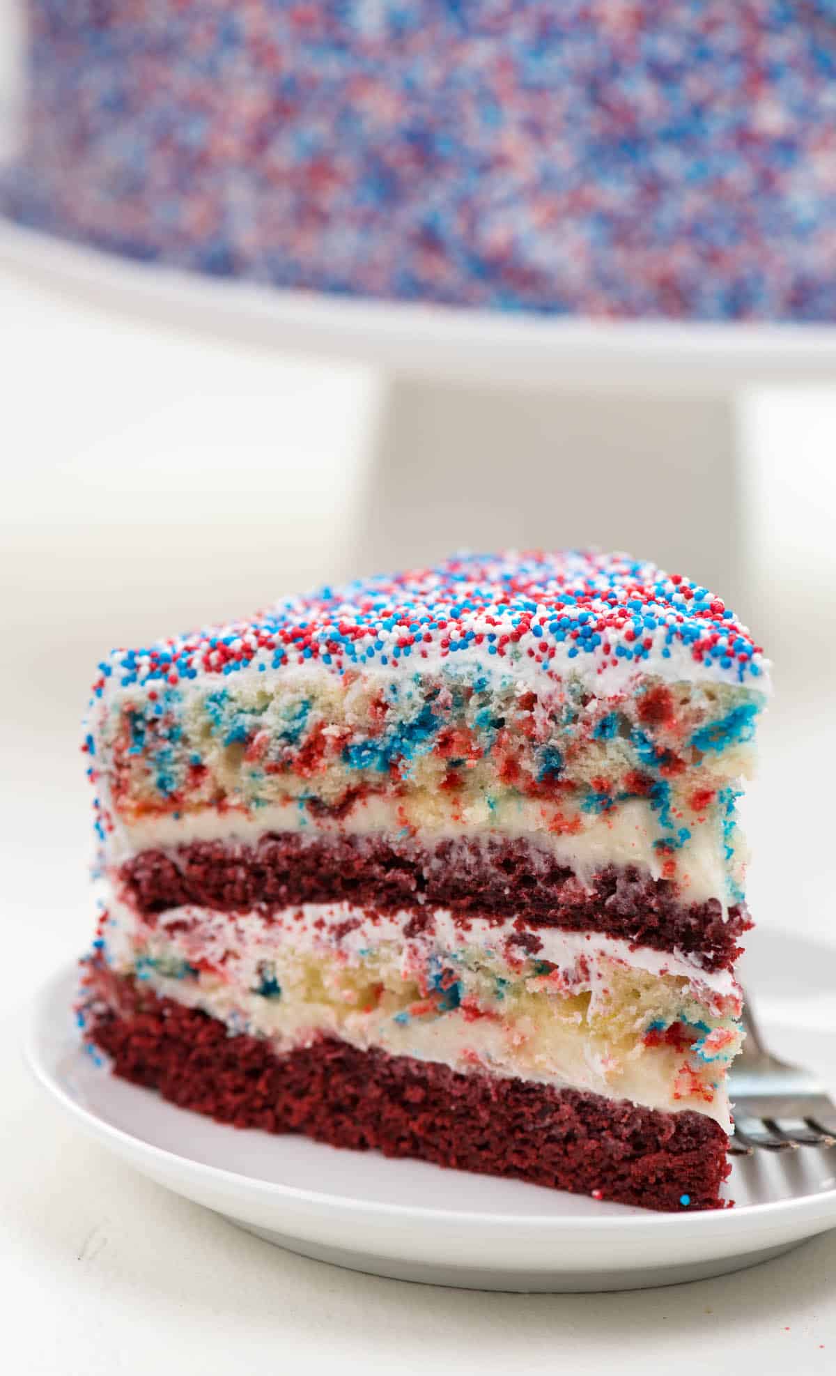 yellow and red layered cake covered in patriotic sprinkles on a white plate.