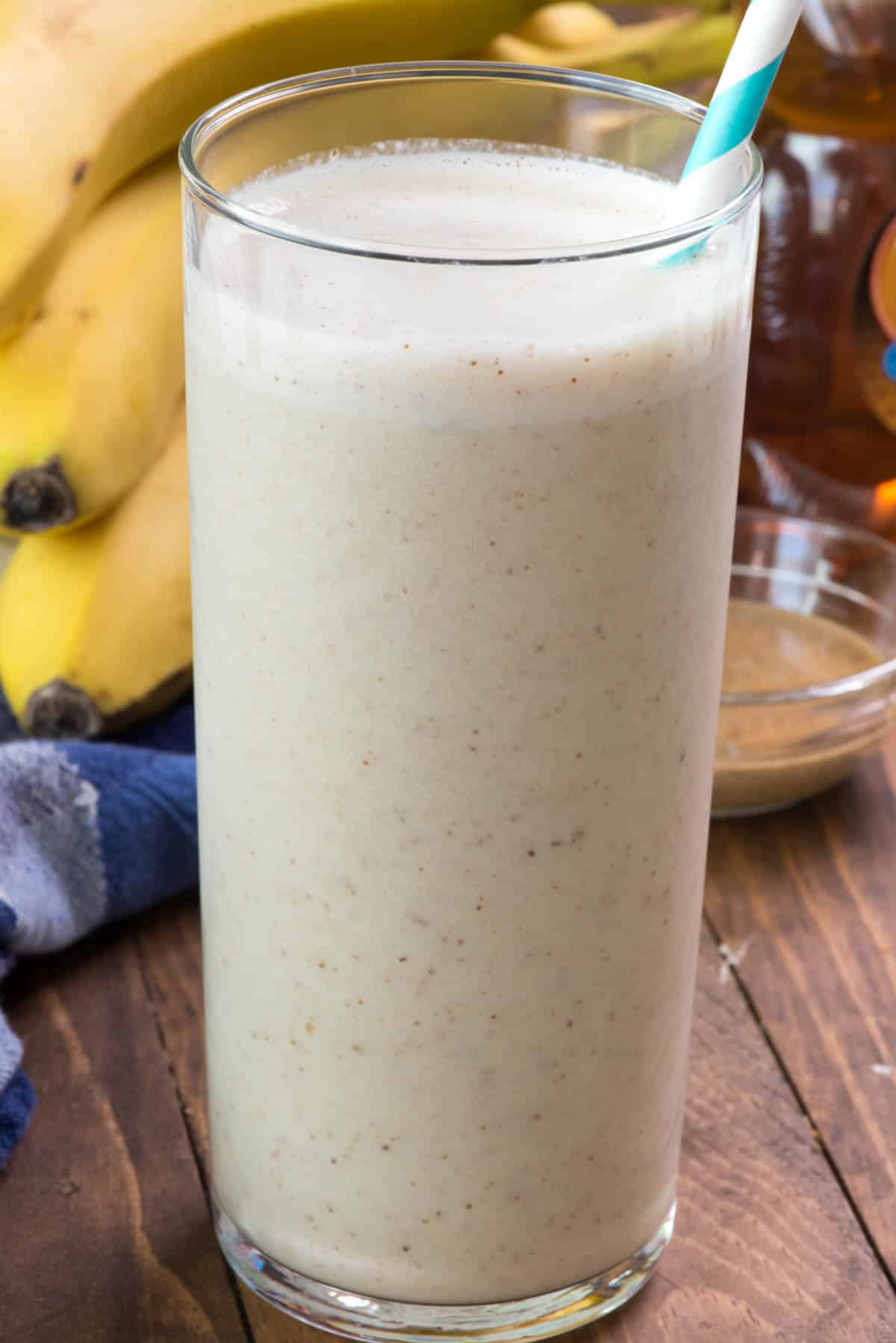 smoothie in a tall clear glass with a blue and white swirled straw in the drink.