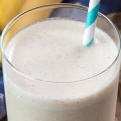 smoothie in a tall clear glass with a blue and white swirled straw in the drink.