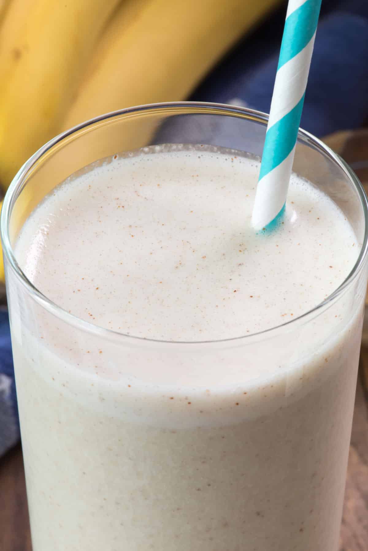 smoothie in a tall clear glass with a blue and white swirled straw in the drink.