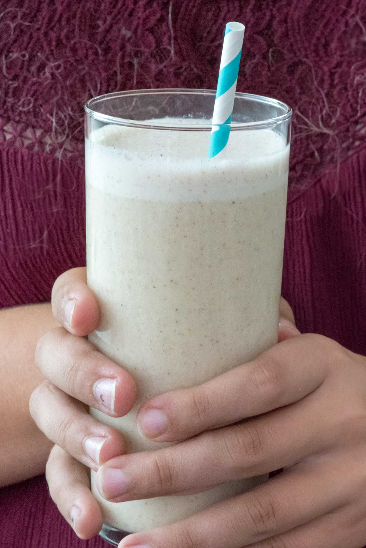 smoothie in a tall clear glass with a blue and white swirled straw in the drink.