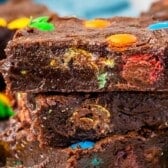 Close-up of two thick, fudgy M&M Brownies stacked, with colorful candy-coated chocolates baked inside and sprinkled on top.